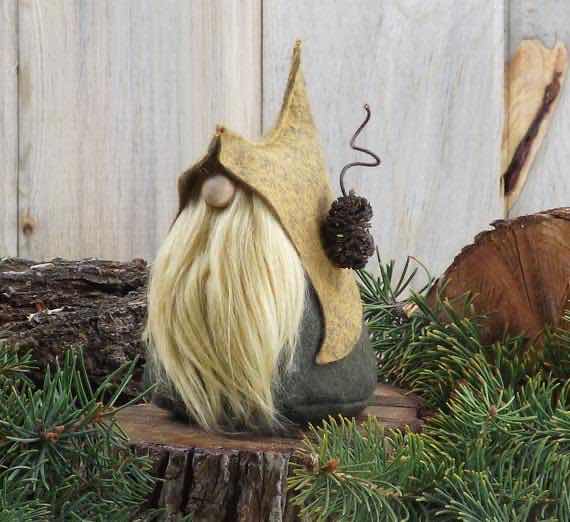 Nim the gnome. He is wearing a large tan hood over an indistinct grey-green garment. He has a large blonde beard, covering everything beneath his nose. Everything above his nose is obscured by the hood. He has a pinecone stuck to his hood. He is visually identical to Lore the Quirky, a creation of TheGnomeMakers on Etsy.